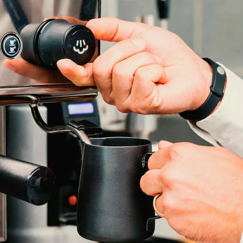 Person using an espresso machine to fill a black mug.