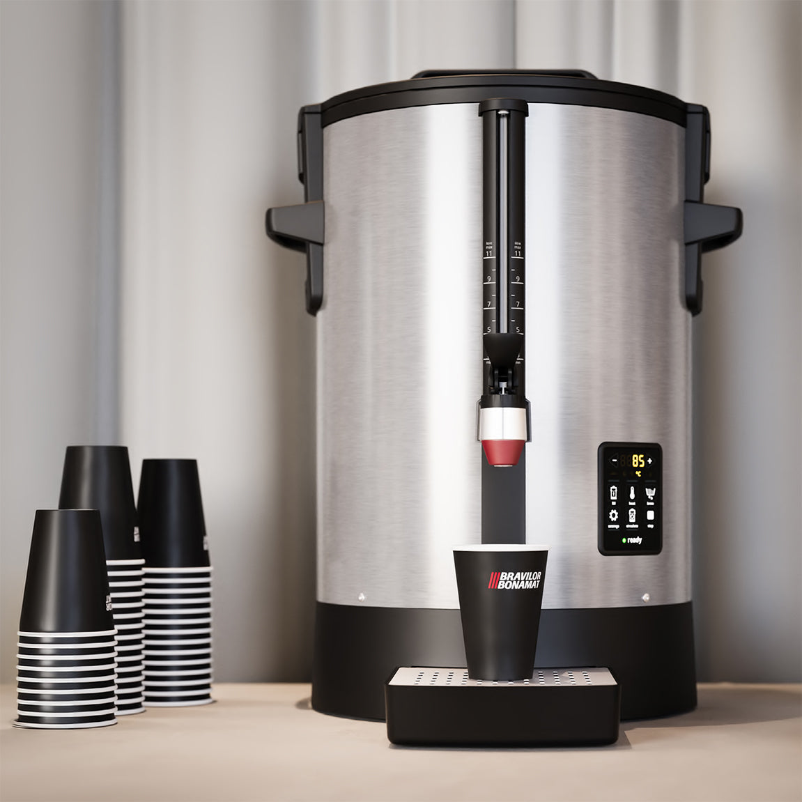 Large coffee urn with digital display and black and white striped cups on a neutral background