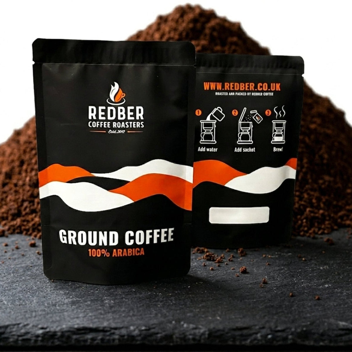 Two black coffee bags with red and white design on a dark surface with coffee grounds.