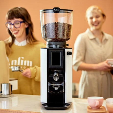 Coffee grinder with coffee beans on a kitchen counter, two people in the background.