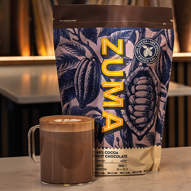Zuma hot chocolate bag with a mug of hot chocolate on a surface.