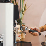 Person using a coffee machine with a focus on the hand and coffee grinder.