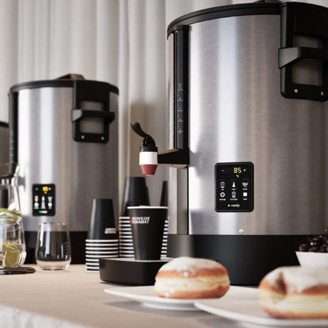 Modern coffee machine on a kitchen counter with donuts and coffee cups.