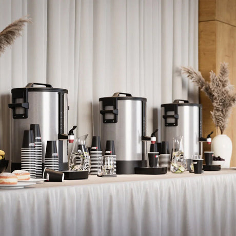 Coffee service setup with urns, cups, and saucers on a table against a striped wall.