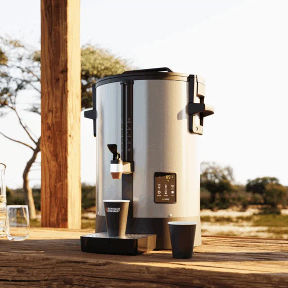 Large coffee urn on a wooden surface outdoors with a scenic background