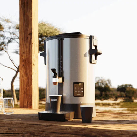 Large coffee urn on a wooden surface outdoors with a scenic background