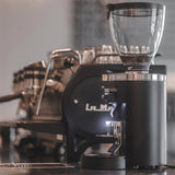 La Marzocco coffee grinder with a blurred background of a coffee shop setting