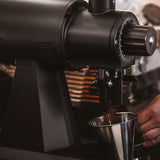 Coffee grinder dispensing coffee into a metal container with a blurred background