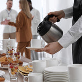People gathered around a table with food and drinks, a person serving coffee.