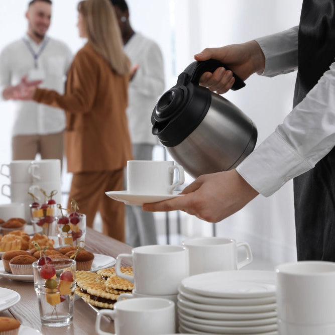 People gathered around a table with food and drinks, a person serving coffee.