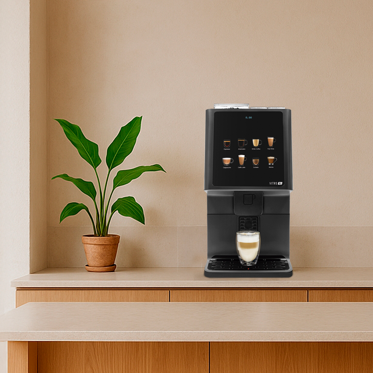 A modern black coffee machine sits on a light wood countertop in a warm, minimalist kitchen or cafe setting with wooden stools, a potted plant, and pendant lights.