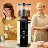 Coffee grinder with coffee beans on a kitchen counter, two people in the background.