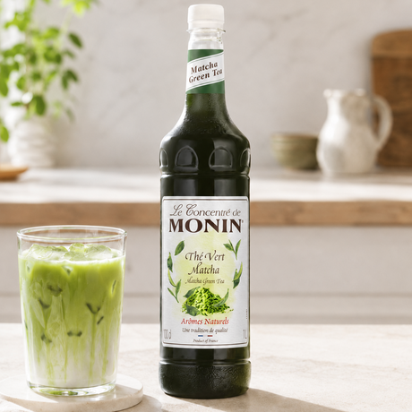 Monin Matcha Green Tea syrup bottle with a glass of matcha green tea on a wooden surface.