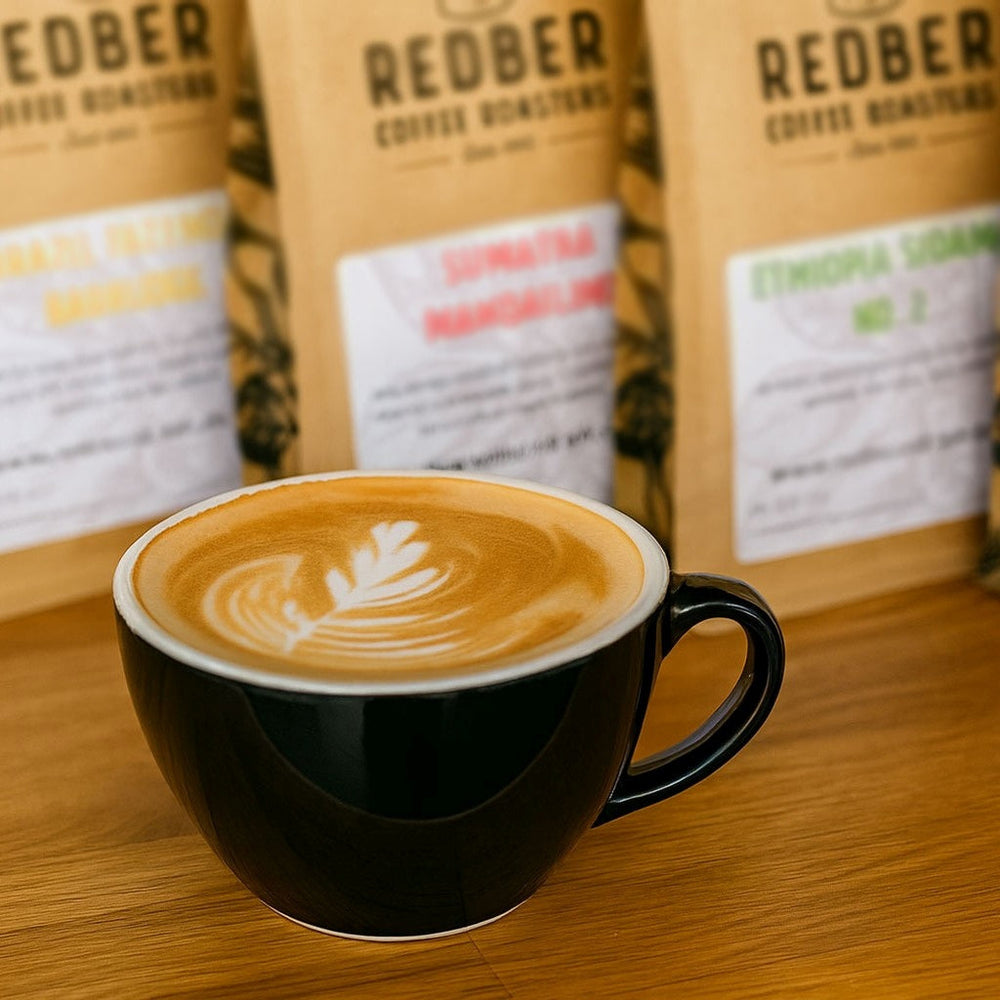 Black coffee cup with latte art in front of Redber coffee bags on a wooden surface