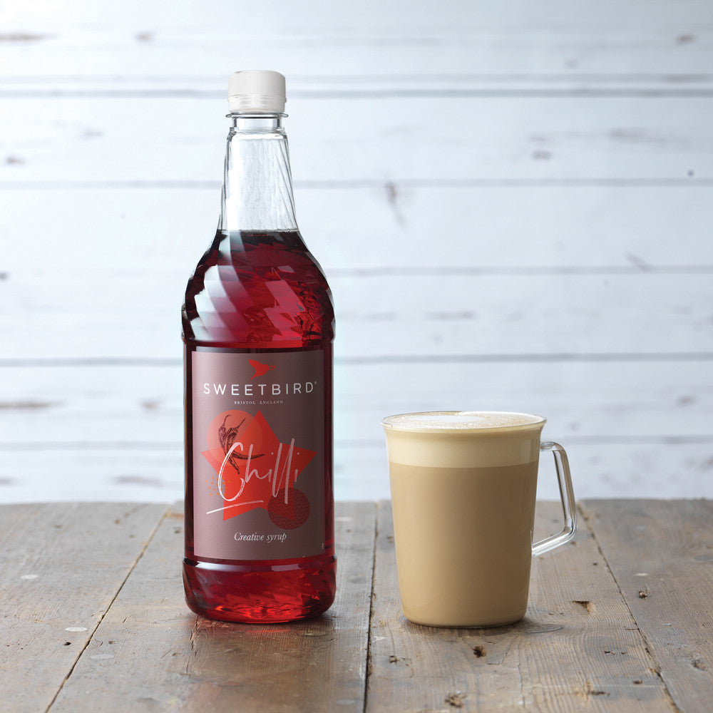 Bottle of Sweetbird syrup next to a cup on a wooden surface with a light gray background