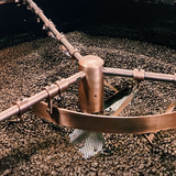 Coffee roasting process with a metal roaster turning coffee beans.