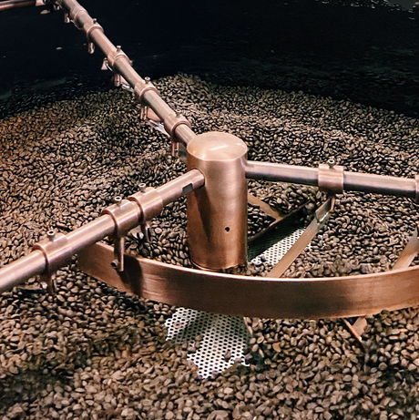 Coffee roasting process with a metal roaster turning coffee beans.