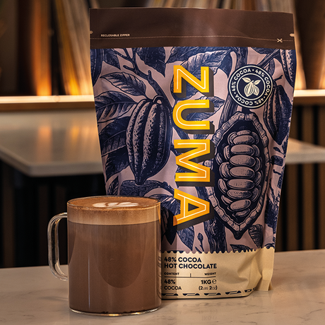 Zuma hot chocolate bag with a mug of hot chocolate on a surface.