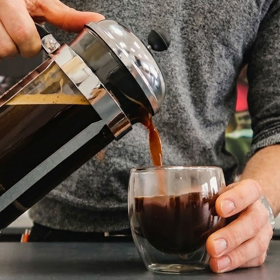 Person pouring coffee from a French press into a glass.