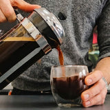 Person pouring coffee from a French press into a glass.