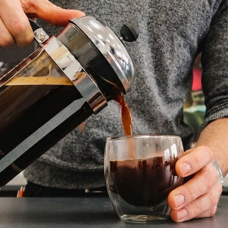 Person pouring coffee from a French press into a glass.
