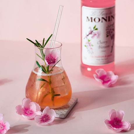 Cocktail with flowers and Monin bottle on a pink background