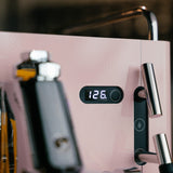 Close-up of a pink coffee machine with a digital display showing '126.' on a blurred background.