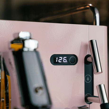 Close-up of a pink coffee machine with a digital display showing '126.' on a blurred background.