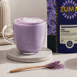 Purple ube powder with a Zuma package and a glass of ube latte on a light surface.