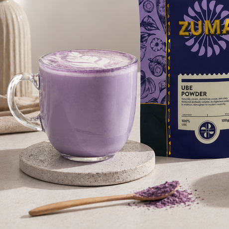 Purple ube powder with a Zuma package and a glass of ube latte on a light surface.